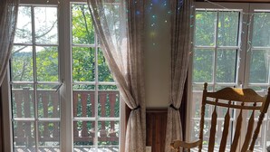A room with a rocking chair, a small table, and a view of a wooden deck through large windows.
