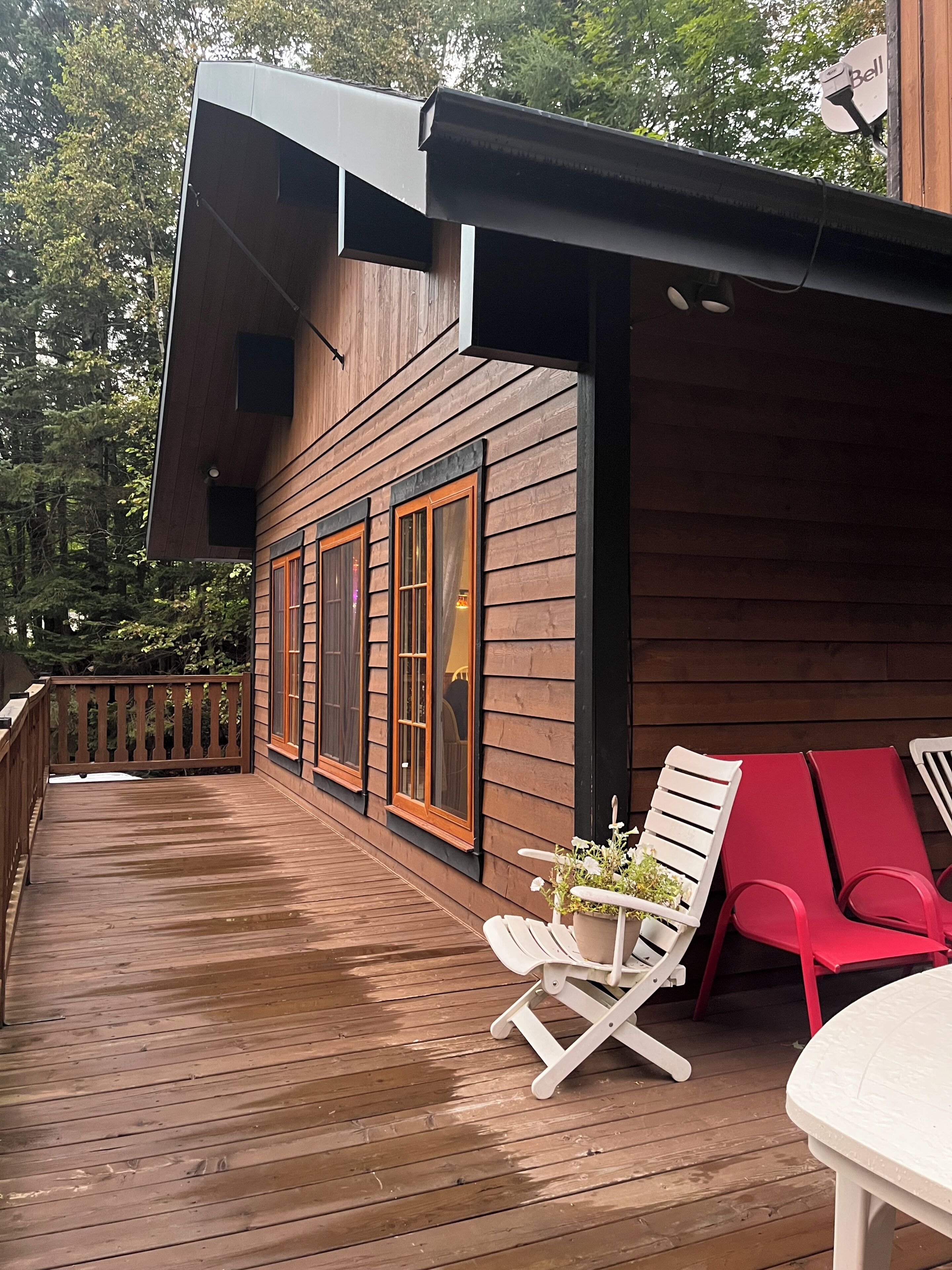 A wooden deck with a railing, a potted plant, and two lounge chairs.