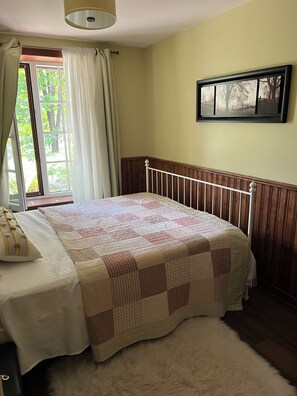 A bedroom with a bed, a window with curtains, a wall-mounted picture, and a fluffy rug. - Cozy Chalet with private SPA in the Laurentians (Sainte-Agathe-des-Monts)