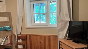 A room with a wooden bunk bed, a desk with a computer, a window with curtains, and a radiator.