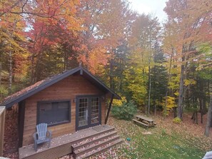 A wooden cabin with a porch, a bench, and a picnic table in a forested area. - Cozy Chalet with private SPA in the Laurentians (Sainte-Agathe-des-Monts)