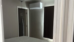 Et soveværelse med en seng, loftventilator, aircondition, en dør og et vindue med gardiner.
