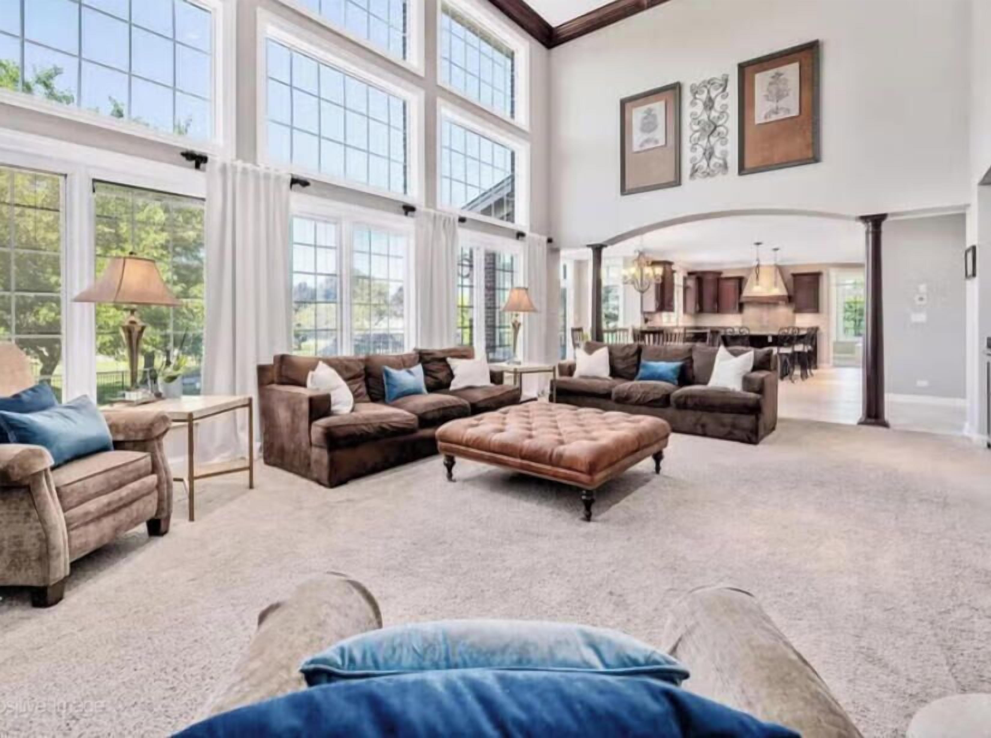 A spacious living room with a large sectional sofa, a matching ottoman, and a dining area in the background.