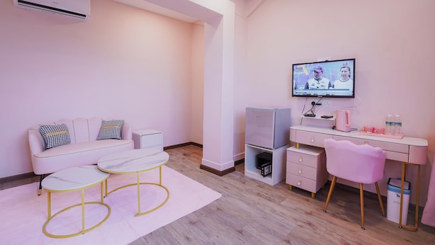 A modern, pink-themed room with a sofa, two chairs, a desk with a computer, a television, and an air conditioning unit. - The Pink Boutique (George Town)