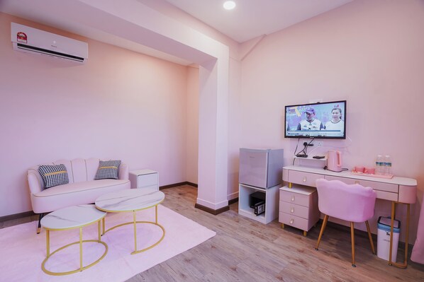 A modern, pink-themed room with a sofa, two chairs, a desk with a computer, a television, and an air conditioning unit. - The Pink Boutique (George Town)