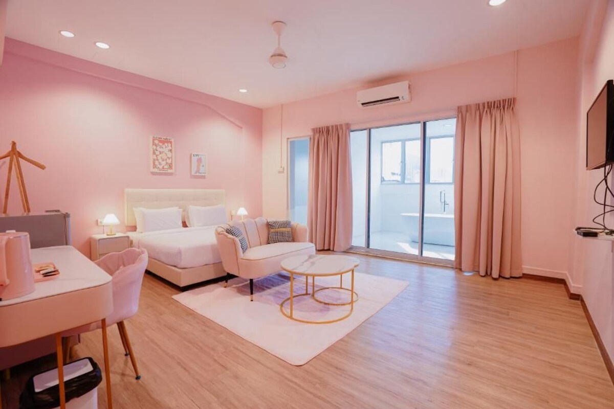 A modern hotel room with a bed, a desk, a chair, a small table, and a large window with curtains.