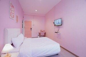 A bedroom with a bed, a bedside table with a lamp, a TV mounted on the wall, and a door leading to another room.