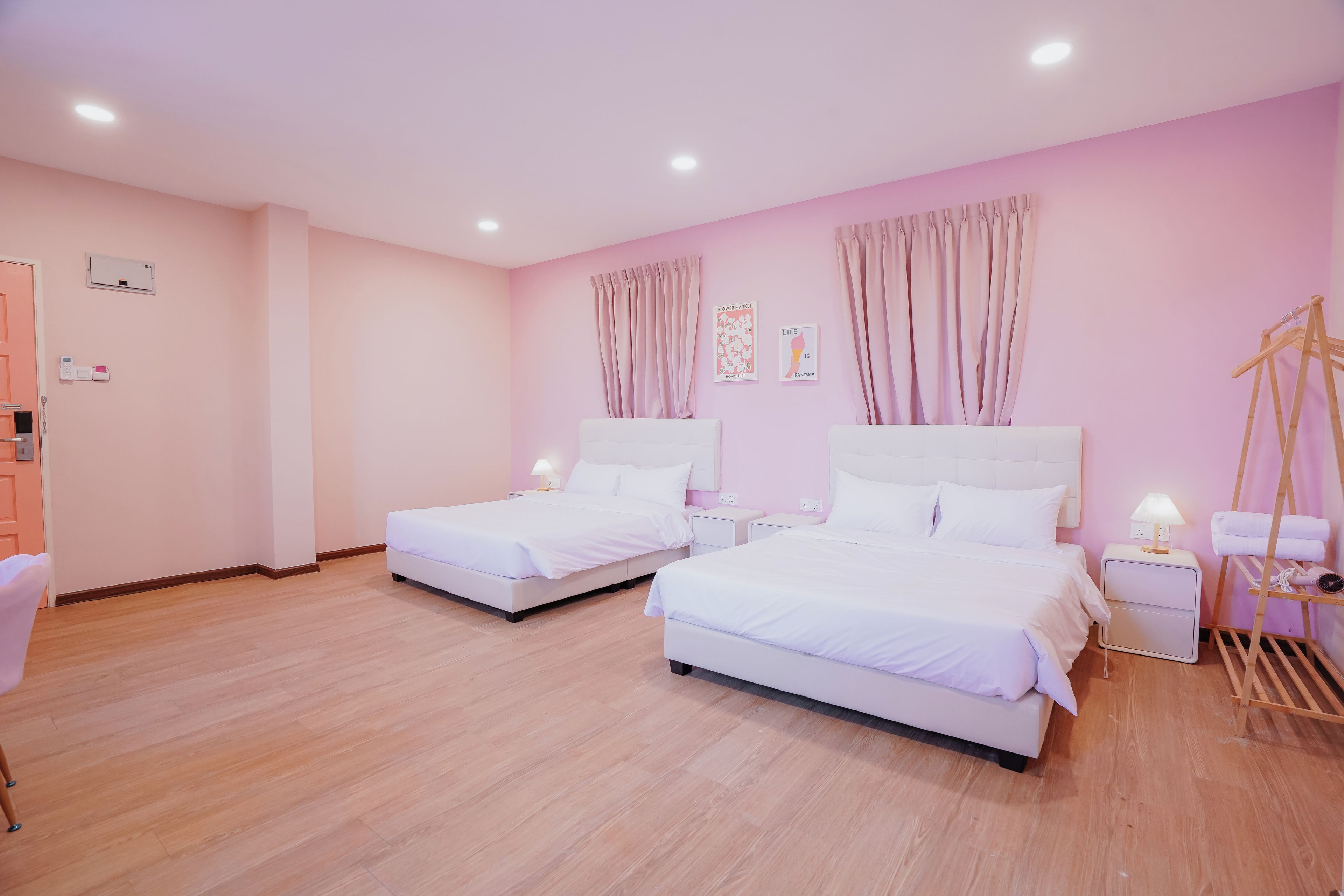 A hotel room with two beds, a wooden floor, a pink wall, and a window with curtains.