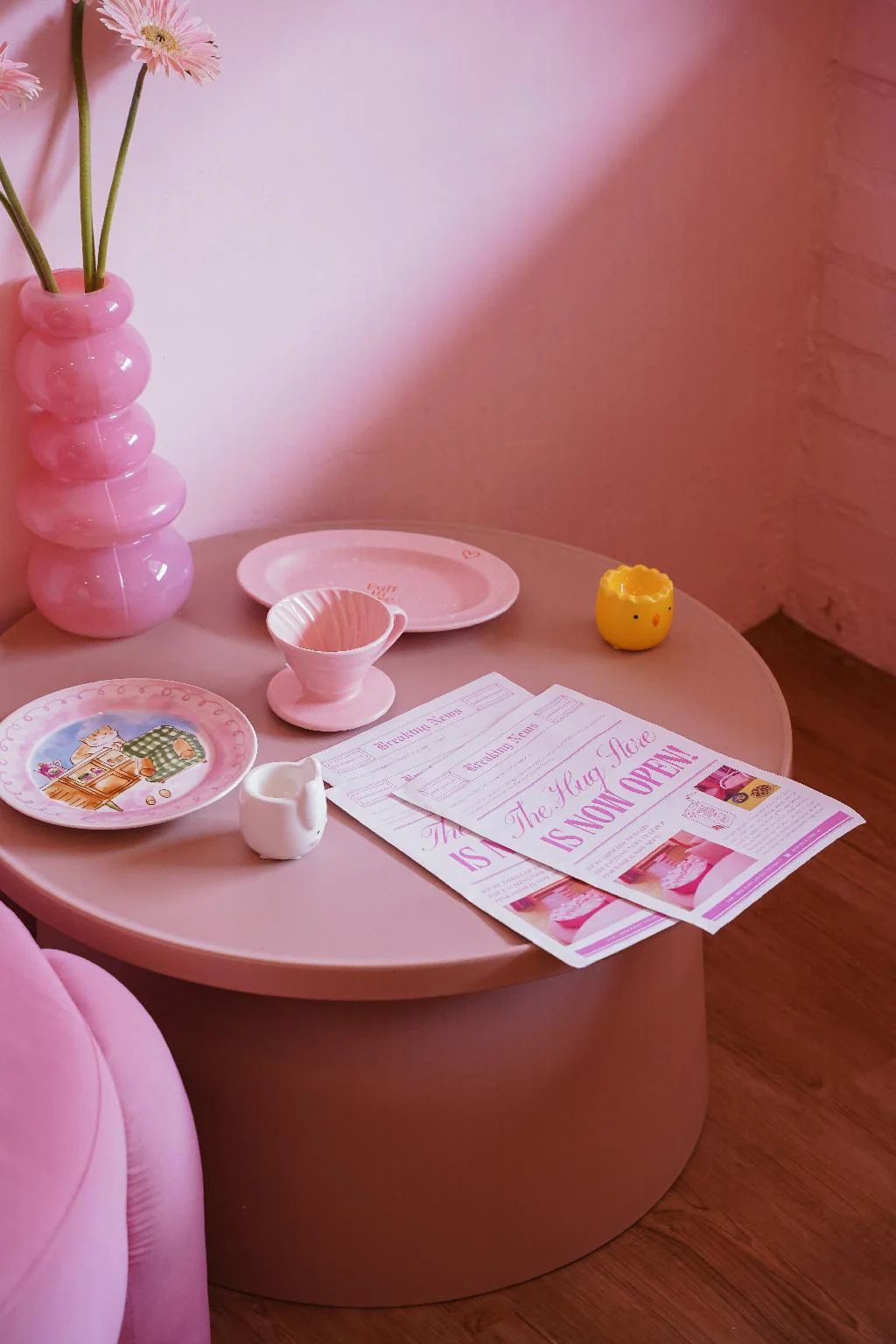 A pink table with a vase, plates, a yellow figurine, and a menu.