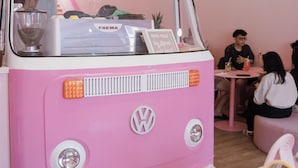 A pink VW camper van interior with a kitchen area, a table, and a hanging light fixture. - The Pink Boutique (George Town)