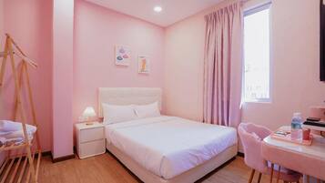 A pink-themed hotel room with a bed, bedside table, lamp, and a chair.