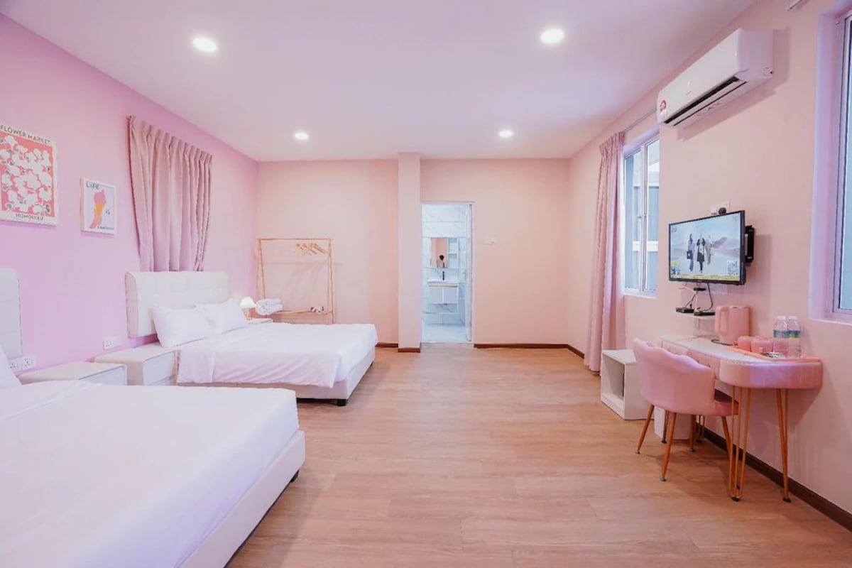 A hotel room with two beds, a desk with a chair, a television, and an air conditioning unit.