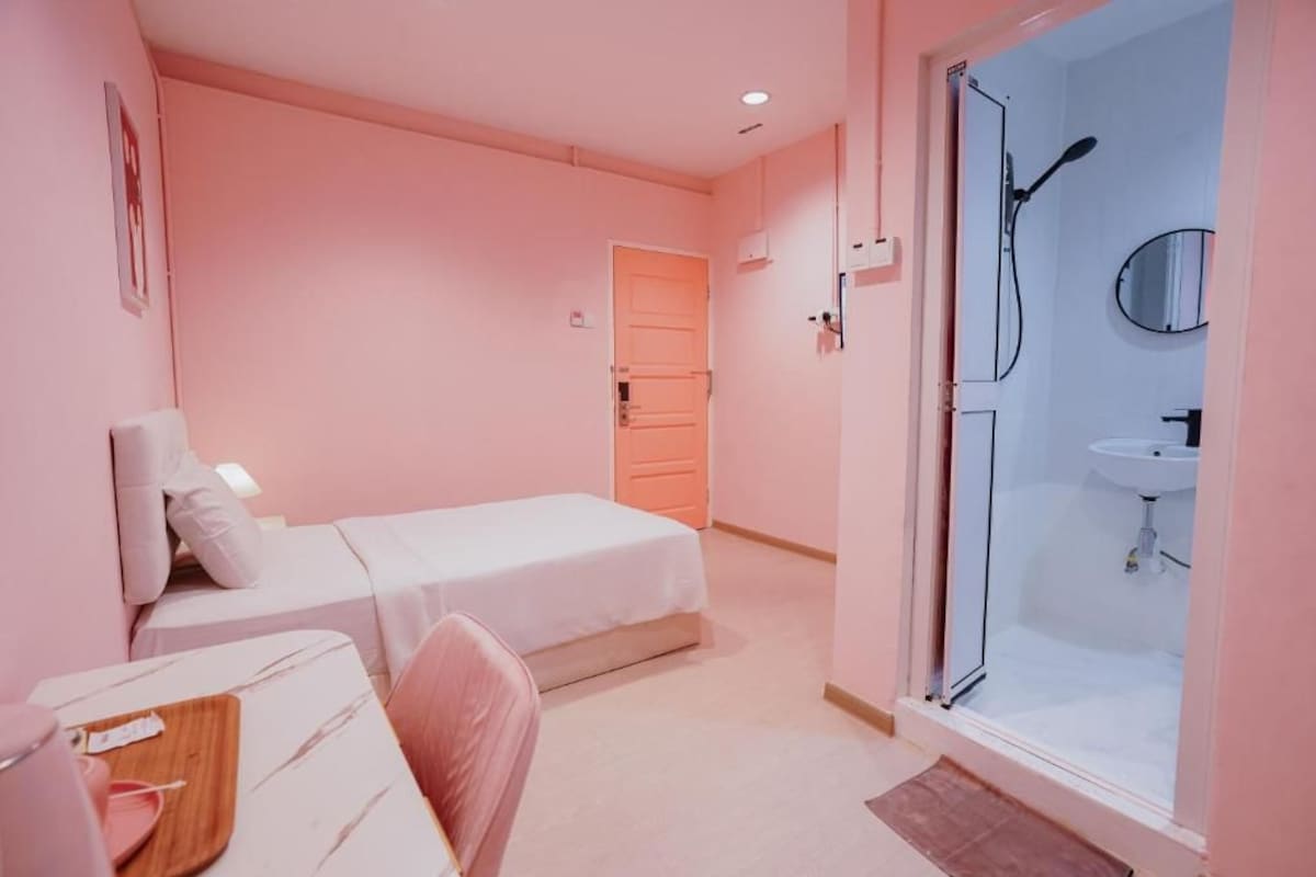A bedroom with a bed, a desk, a chair, a wardrobe, a door, and a bathroom with a shower and sink.