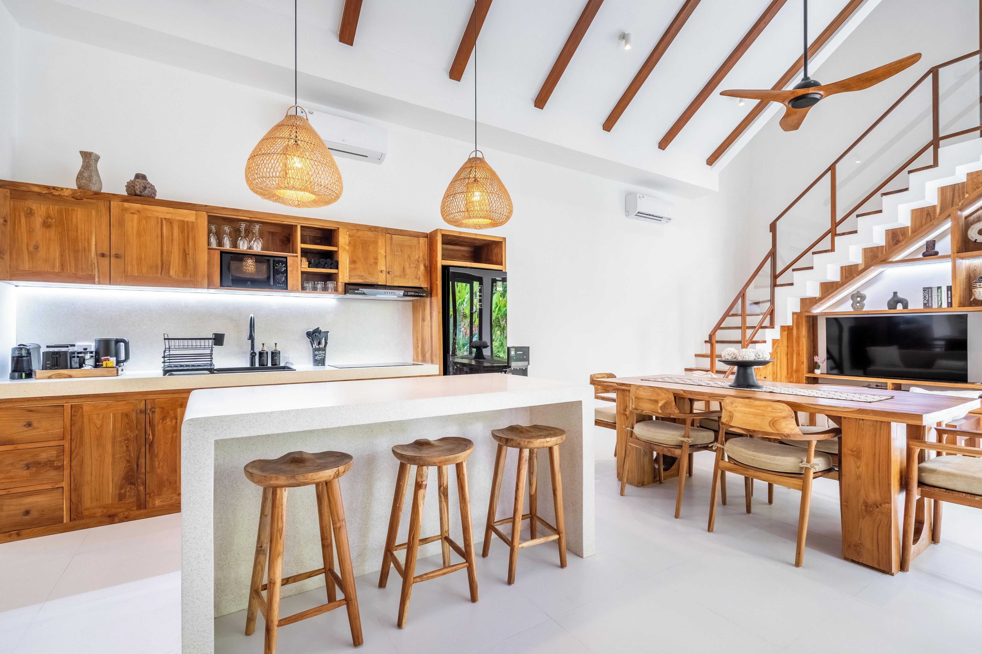Una cocina moderna con armarios de madera, una isla central con taburetes y una escalera que lleva a una zona superior.