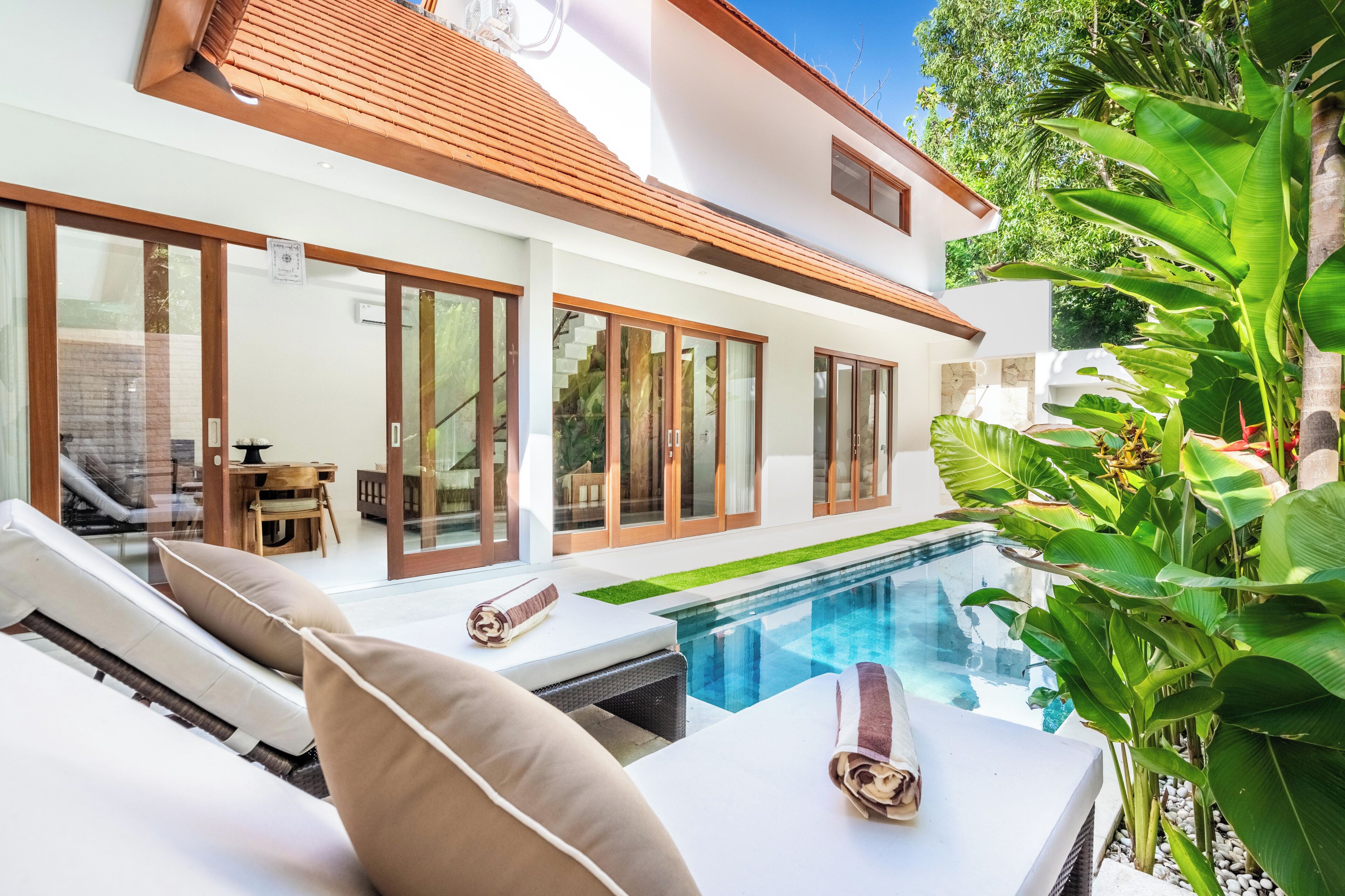 Une maison moderne dotée d’une piscine, de grandes fenêtres et d’un patio avec des chaises longues.