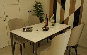 A dining table with chairs, a bottle of wine, a glass, and a bowl of fruit.