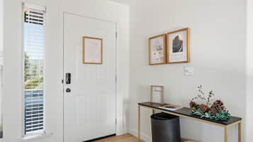 A white door with a notice, a framed welcome sign, a small table with a plant, and a trash bin.