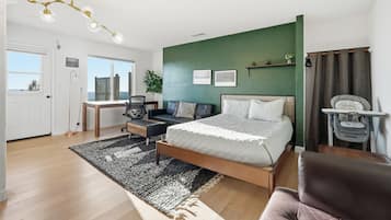 A bedroom with a bed, a desk, a chair, a sofa, a window, and a green wall.