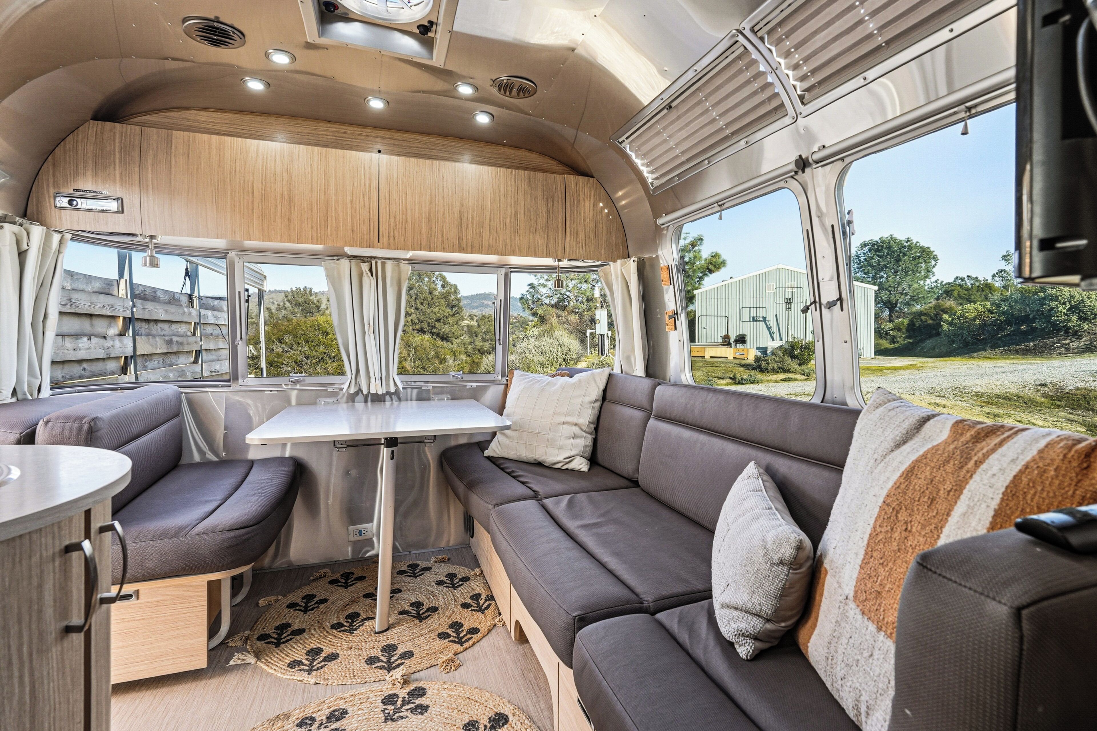 A modern RV interior with a dining area, seating, and a view of the outdoors.