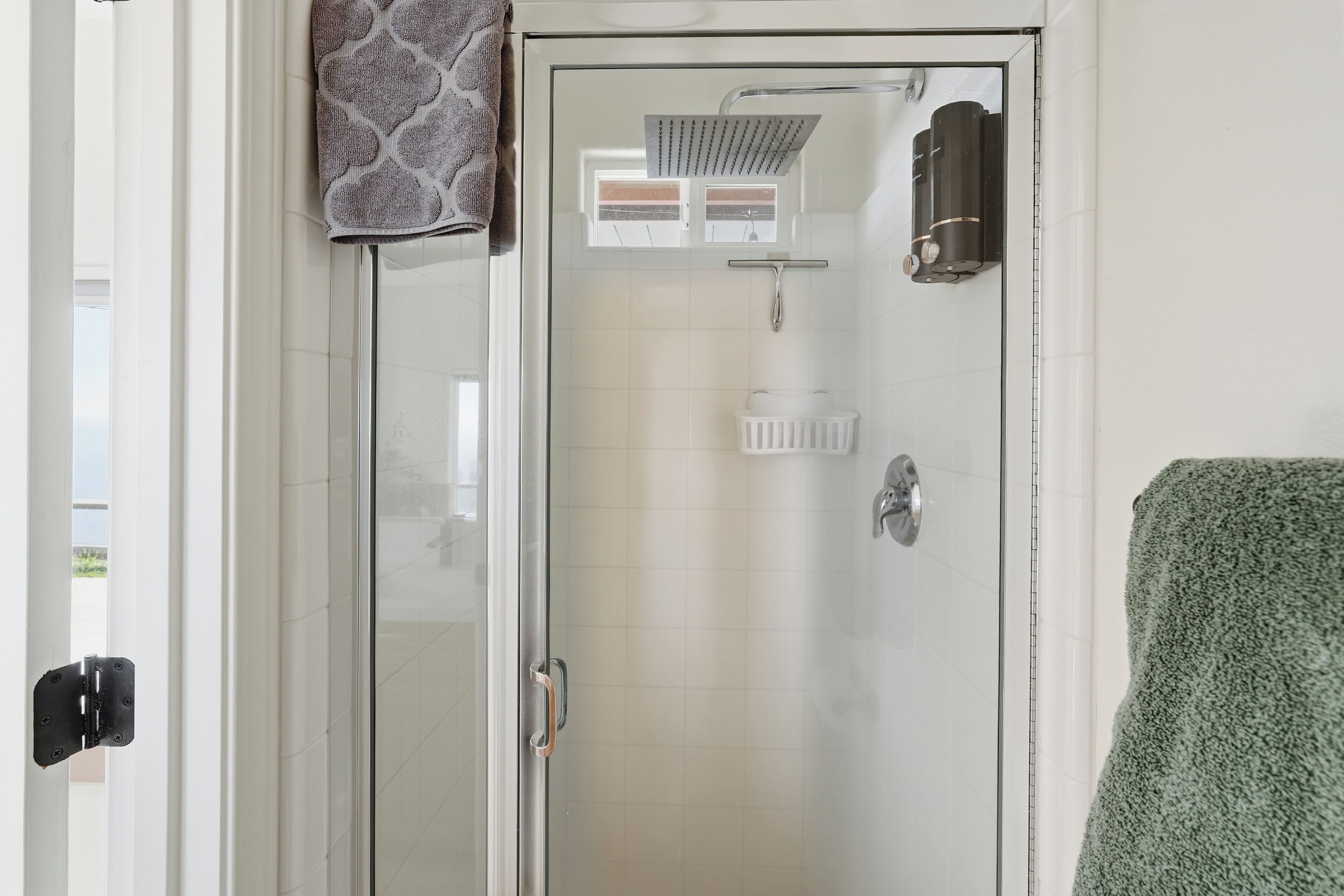 A glass-enclosed shower with a handheld showerhead, a towel rack, and a toilet paper holder.
