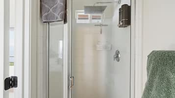 Une douche fermée par des parois en verre, dotée d’un pommeau de douche à main, d’un porte-serviettes et d’un support à papier toilette.