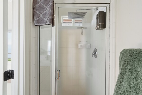 A glass-enclosed shower with a handheld showerhead, a towel rack, and a toilet paper holder.