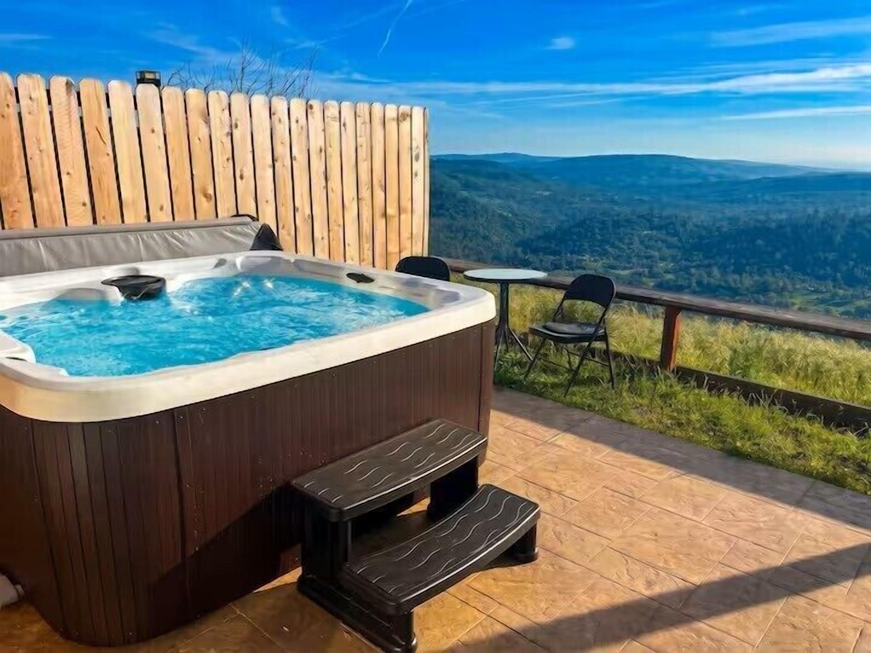 A hot tub on a wooden deck with a view of a forested landscape.