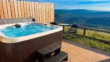 A hot tub on a wooden deck with a view of a forested landscape.