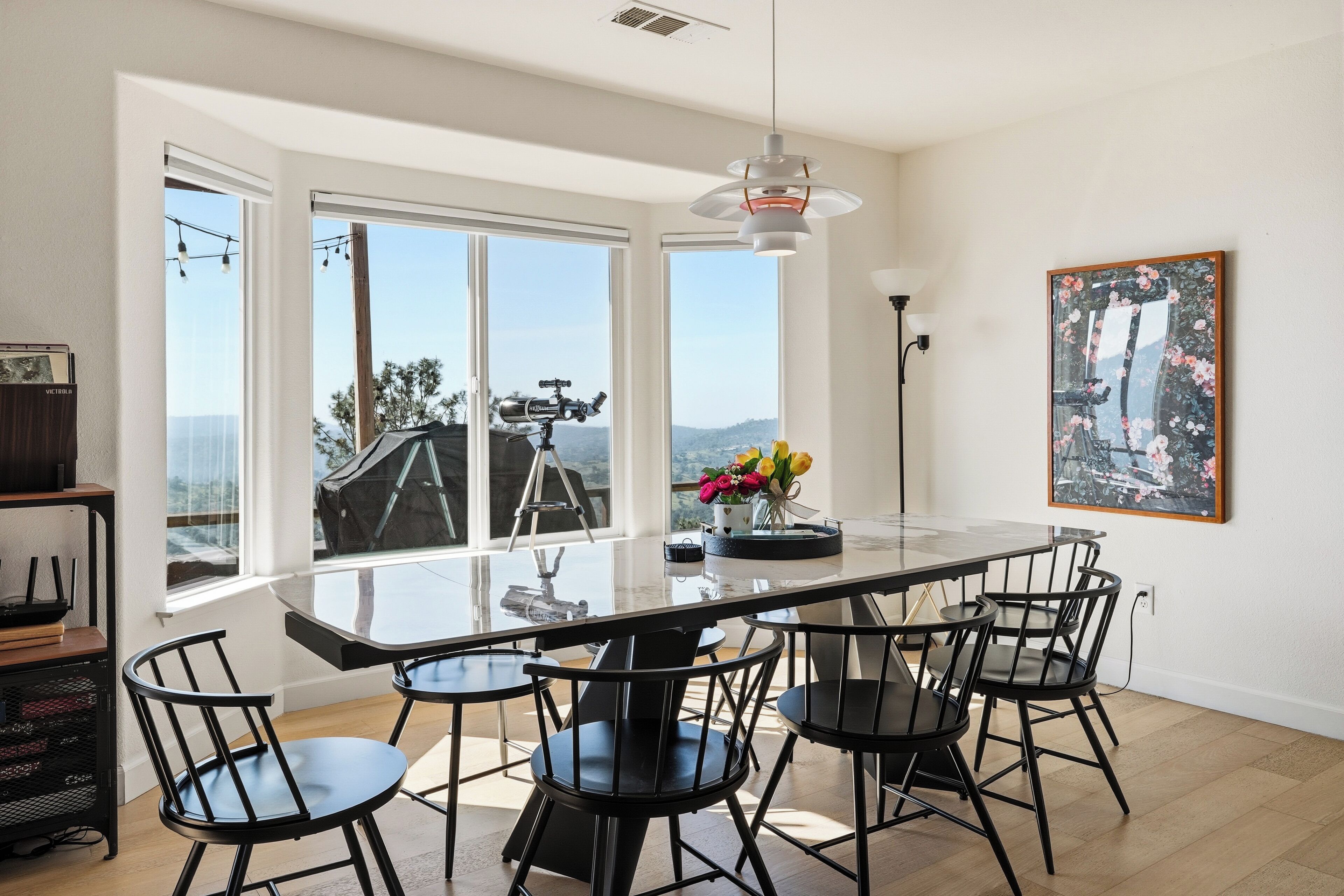 Un comedor moderno con una mesa de vidrio, sillas negras y un ventanal con vistas al exterior.