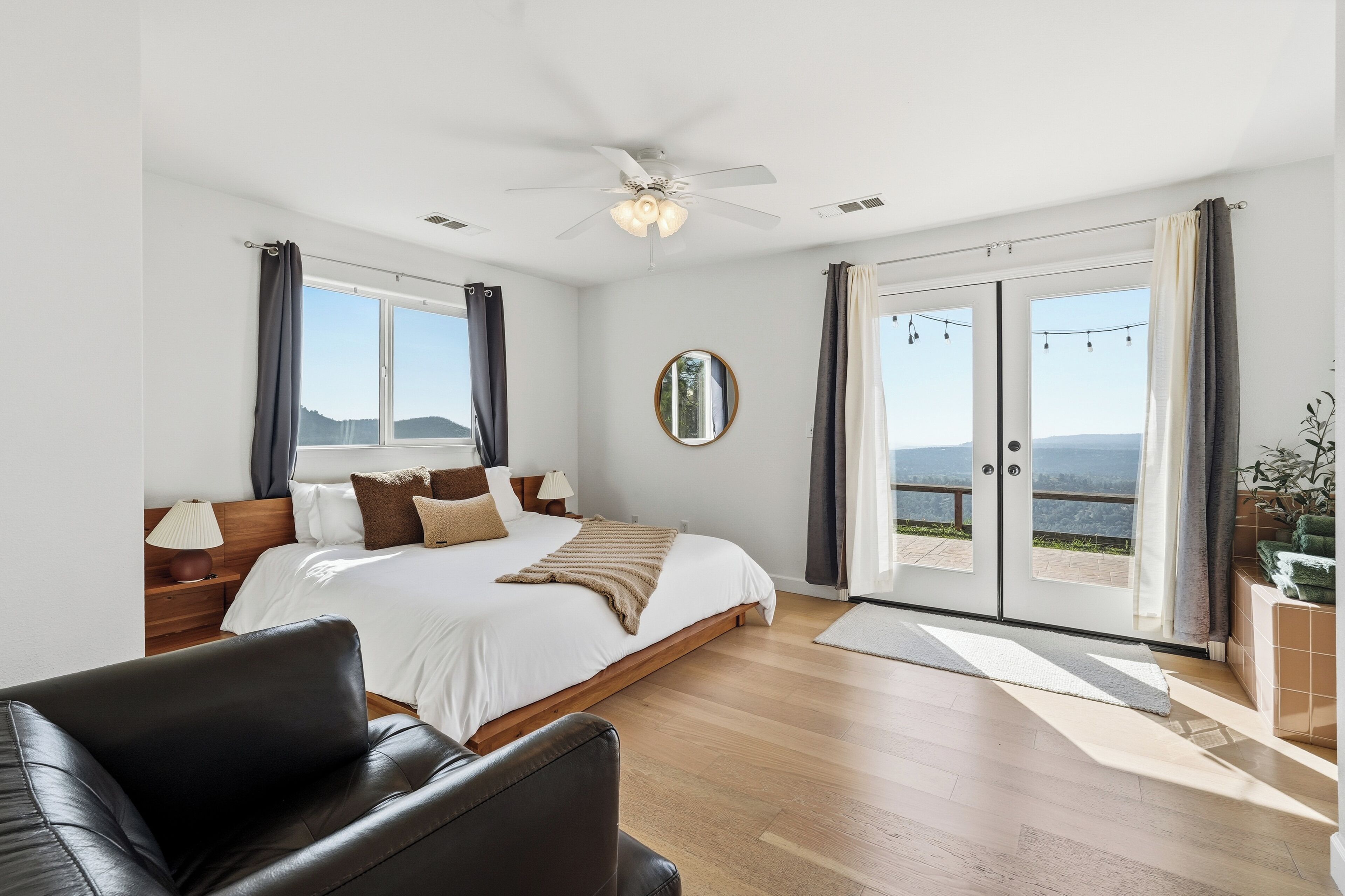 A bedroom with a bed, a ceiling fan, a large window, and a view of the outdoors.