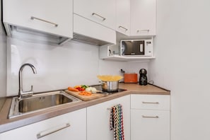 A modern kitchen with a stainless steel sink, a microwave, a coffee maker, and a cutting board with vegetables.
