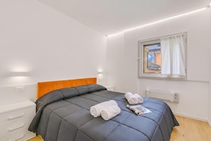 A bedroom with a bed, a window with curtains, a radiator, and a white dresser.