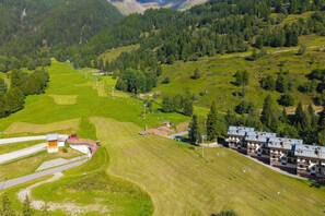 A mountainous landscape with a ski resort, including a building with multiple balconies and a parking area. - Ski In-Ski Out Apartment in Peio Val di Sole, Peio, Italy (Peio)