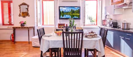 A dining area with a table set for four, a television mounted above the table, and a kitchen area with modern appliances.