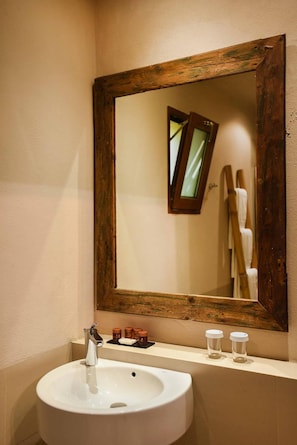 Un baño con un lavamanos blanco, un espejo con marco de madera y un estante con artículos de tocador.