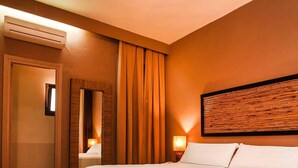 Hotellihuone, jossa on suuri sänky, peili, ovi ja seinälle kiinnitetty taideteos.