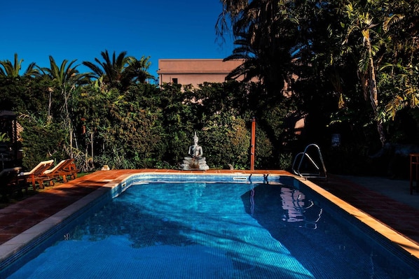 Una piscina con una estatua en el centro, rodeada de palmeras y un edificio al fondo.