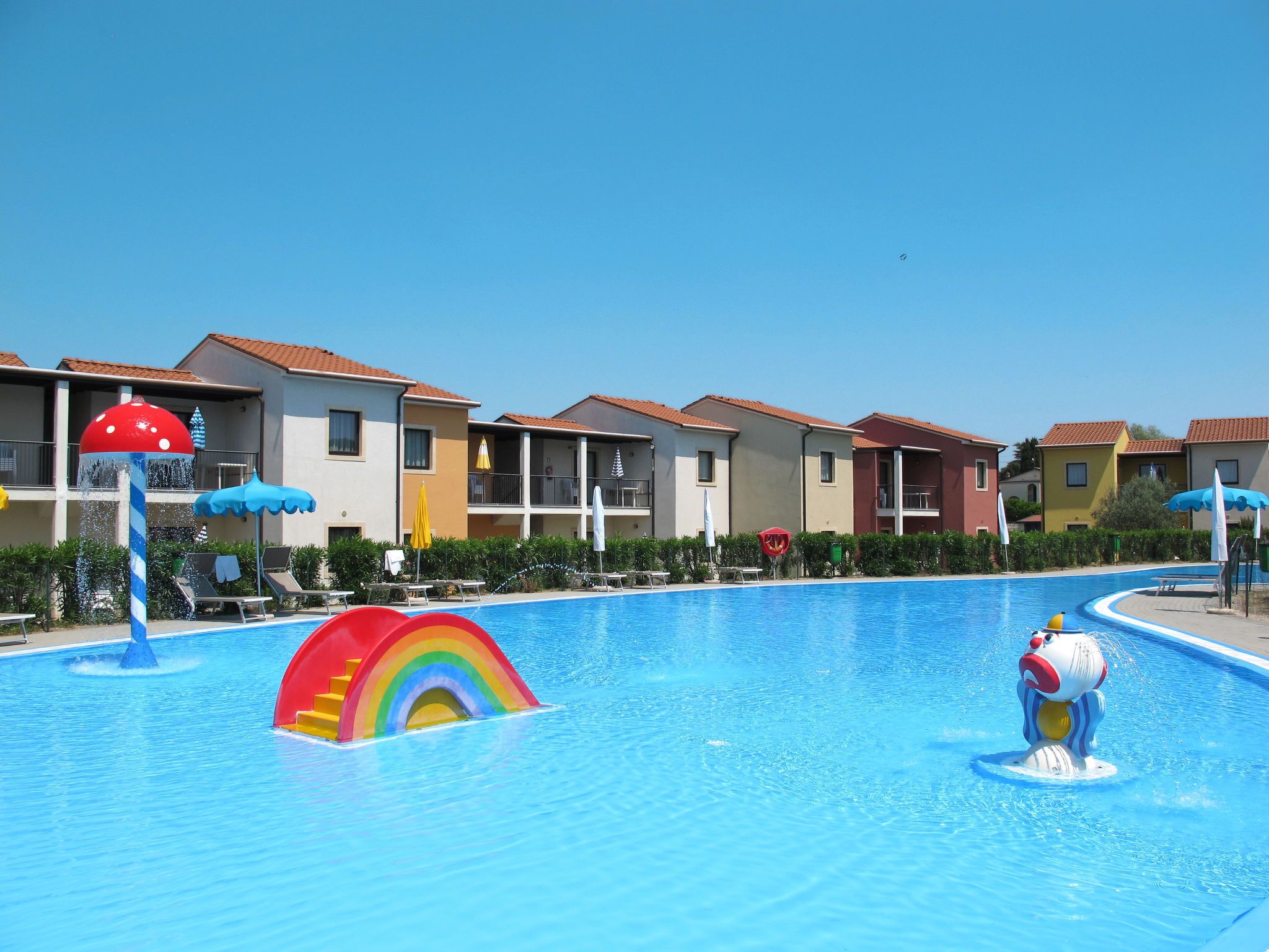 A swimming pool with colorful water features, surrounded by multi-story buildings with balconies and outdoor seating.
