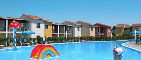 A swimming pool with colorful water features, surrounded by multi-story buildings with balconies and outdoor seating.