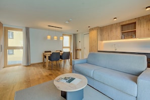 A modern living room with a sofa, a round coffee table, and a dining area with chairs and a table.