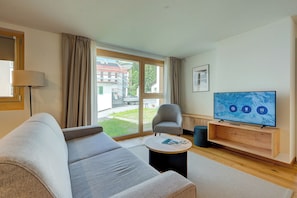 A modern living room with a sofa, armchair, and a flat-screen TV on a wooden stand.