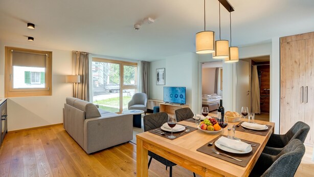 A modern living room with a dining area, a sofa, a television, and a view of the outside.