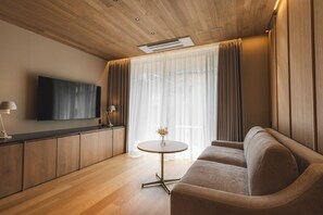 A modern living room with a sofa, a flat-screen TV, a small round table, and a kitchen area with wooden cabinets.