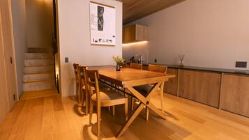 A modern kitchen with wooden cabinets, a dining table with chairs, and a staircase leading to another level.