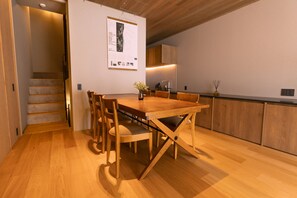 A modern kitchen with wooden cabinets, a dining table with chairs, and a staircase leading to another level.