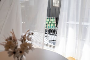 A room with a view of a balcony, a chair, and a table with a vase of dried flowers. - ALMOND HOTEL SHIBUYA F (Shibuya-ku)