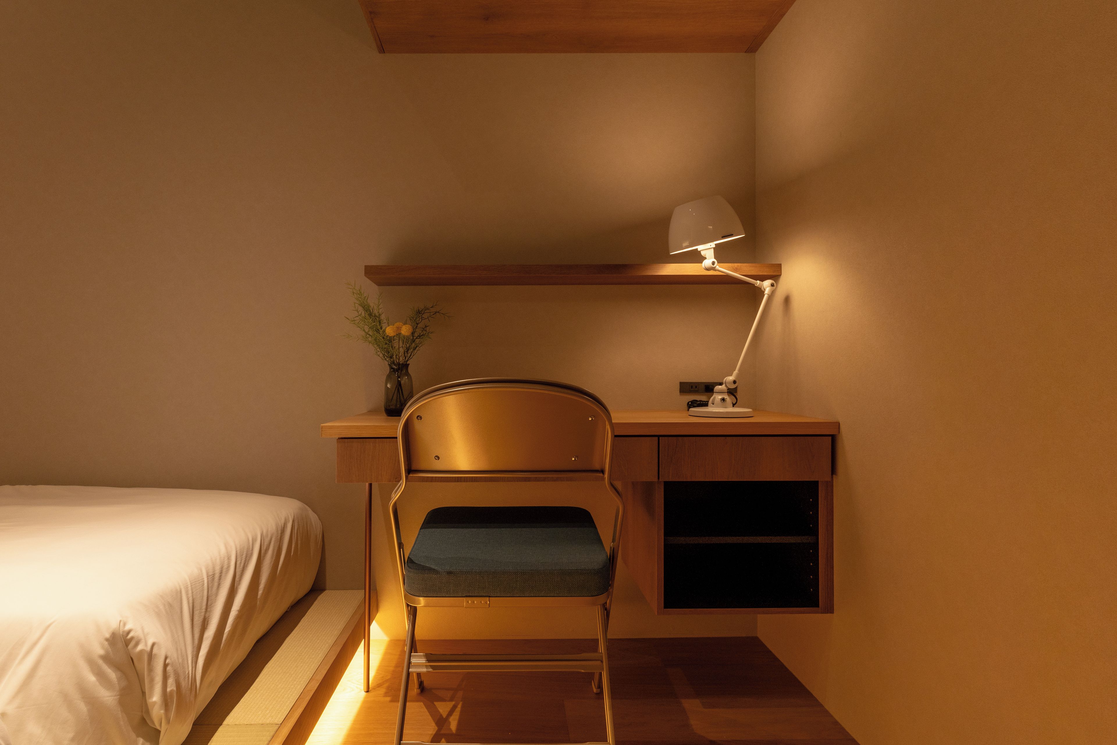 A compact room with a bed, a desk with a chair, and a desk lamp.