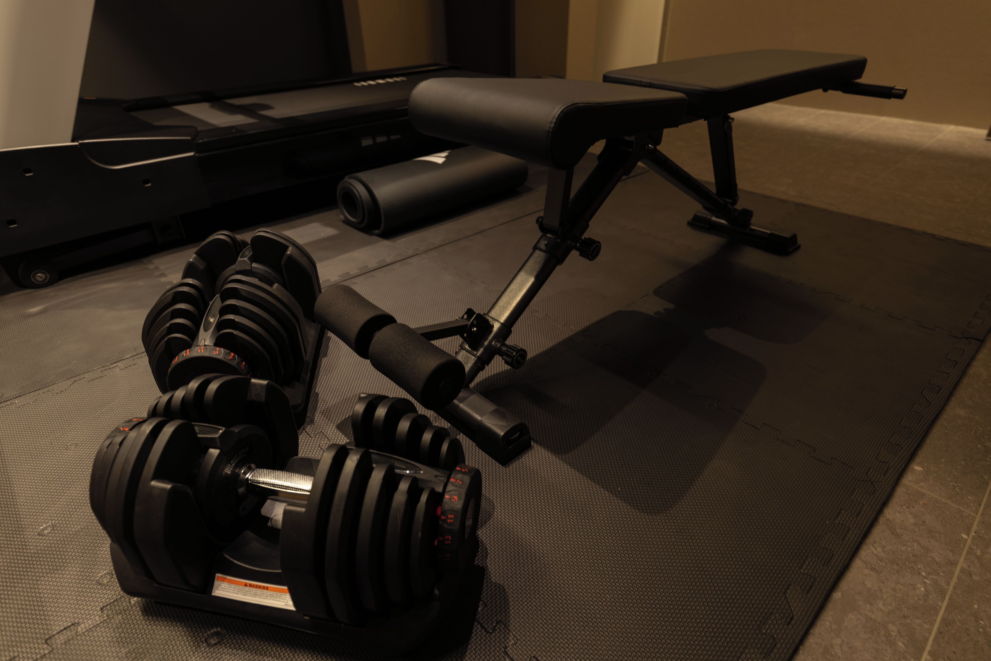A gym with exercise equipment including dumbbells, a bench, and a yoga mat.