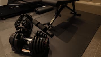 A gym with exercise equipment including dumbbells, a bench, and a yoga mat.