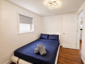 Ein Schlafzimmer mit einem Bett, einem Fenster mit Jalousien, einer Tür und einer Lampe.